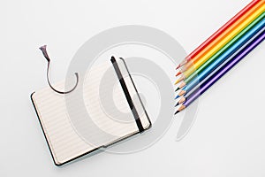 Clean notepad and rainbow color pencils in the shape of an arrow on a white background top view copy space