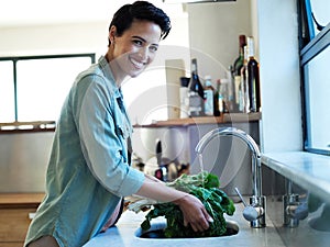 Clean now, delicious later. Portrait of a smiling young woman washing vegetables in her kitchen sink.