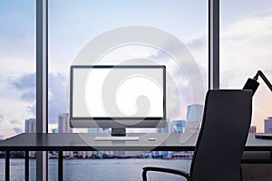 Clean office interior with empty white computer monitor on desk and panoramic windows with beautiful city view and daylight. Mock