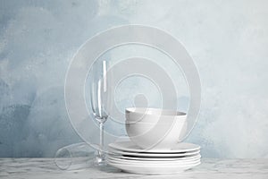 Clean plates, bowls and glasses on marble table against light blue background. Space for text