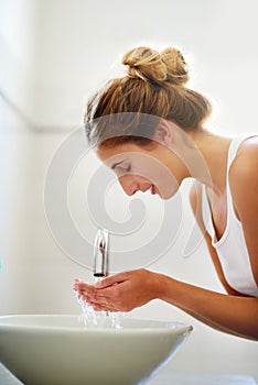 Clean skin is healthy skin. Shot of a beautiful young woman washing her face in the bathroom at home.