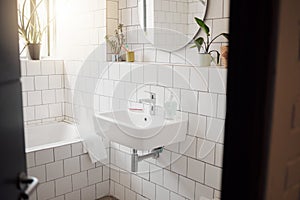 A clean and tidy bathroom inside a house. A basin, bath, with ceramic tiling and a round mirror hanging on the wall. A