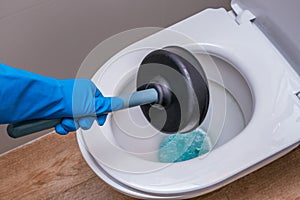 A clean toilet with cleaning agent and a gloved hand with a plunger. The concept of the home cleaning
