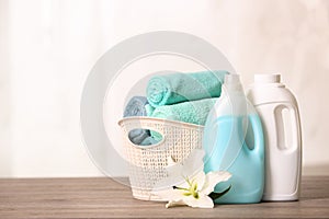 Clean towels in basket with lily and detergents on table