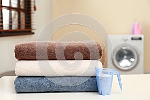 Clean towels and measuring cup of washing powder on table in laundry room