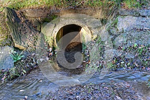 Clean transparent water flowing from concrete drainage pipe into a stream