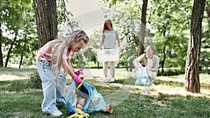 Clean up day with family. Cute little girl holding trash bag and collecting garbage while cleaning with parents in the