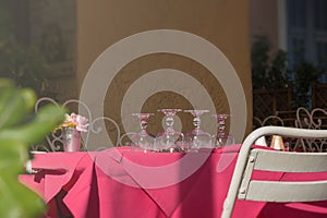 Clean upturned wine glasses on a pink tablecloth. Table setting. Empty restaurant terrace, siesta