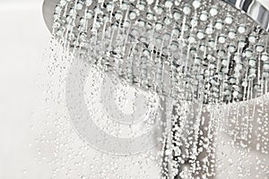 Clean water drops pours from the shower head in the light bathroom