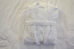 Clean folded bathrobe on white bed.