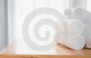 Clean white towels fold on wood table with blurred white bathroom background