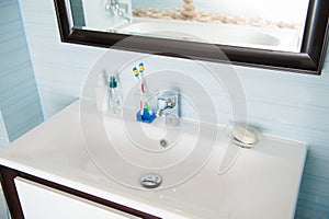 Clean white washbasin with soap and toothbrush in blue bathroom decor with mirror