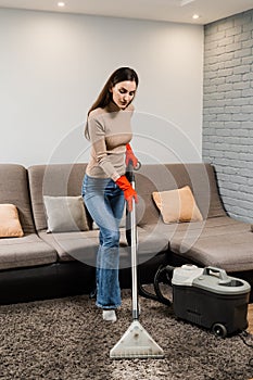 Cleaner girl is cleaning carpet with mop extraction machine for dry clean upholstered furniture. Housekeeper is