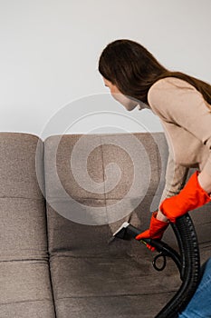 Cleaner girl is cleaning couch with extraction machine for dry clean upholstered furniture. Housekeeper is extracting