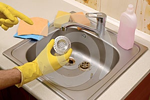 Cleaner in rubber gloves shows clean plughole protector of a kitchen sink