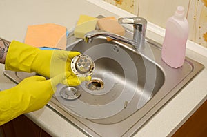 Cleaner in rubber gloves shows waste in the plughole protector of a kitchen sink