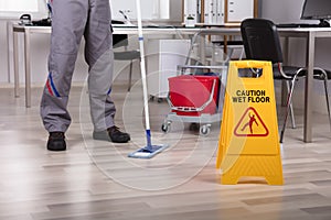 Cleaner Standing With Mop And Caution Wet Floor Sign