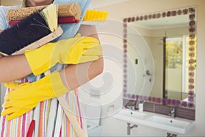 Cleaner wearing washing up gloves and an apron holding broom against bathroom background