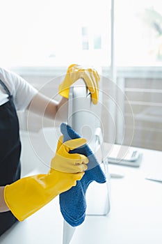 Cleaner is working, Wear rubber gloves and an apron to work, Cleaning staff wiping down office equipment, Wipe the monitor clean