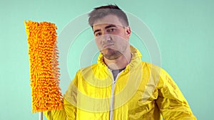 A cleaner in a yellow suit and blue gloves holds a mop in his hand on a blue background, the man nods his head