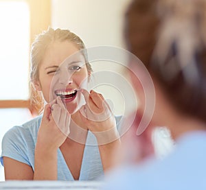 Cleaning all those hard to reach places. a young woman flossing her teeth in a mirror.