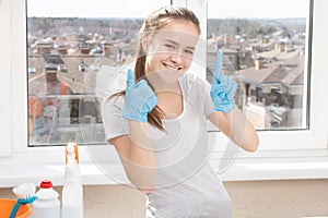 Cleaning of apartments, offices, cottages, warehouses, garages. Young girl in rubber gloves smiles, shows a clean finger without