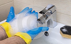 Cleaning the bathroom. hand in a rubber glove washes the wash basin with detergents. soap foam on the hands