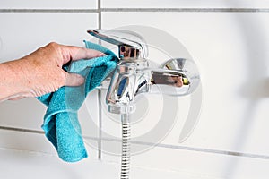 Cleaning a bathtub faucet with a blue microfiber cloth to remove limescale stains from hard calcium water, copy space, selected