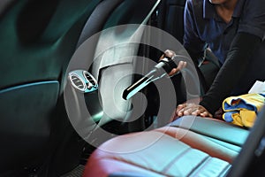 Cleaning car concept. Back seat of luxury car with worker holding car interior vacuum cleaner for cleaning of interior back seat