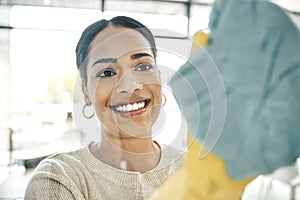 Cleaning, chores and cleaner wiping windows with a soft cloth while wearing gloves in office. Smiling, young and female