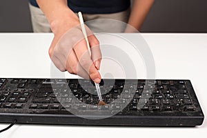 Cleaning computer keyboard in office with rubber protective glove and a brush, dusty and dirty electronic, housework