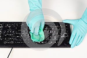 Cleaning computer keyboard in office with rubber protective glove, whiping with water and soap, cleaning dusty and dirty