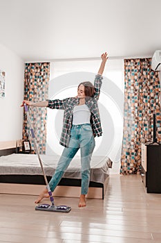 Cleaning concept. Beautiful young brunette woman doing cleaning, dancing with a mop. Room on the background. Vertical orientation