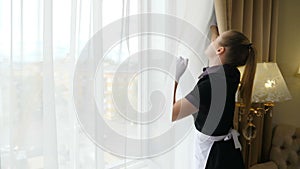 Cleaning concept in hotel. Aeration and ventilation in room. Housemaid in uniform opening curtain lace, letting light