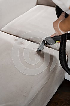 Cleaning couch with washing vacuum cleaner extraction machine for dry clean upholstered furniture. Housekeeper is