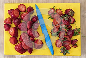 Cleaning, cutting and preparing fresh juicy strawberries with a blue knife in a yellow table