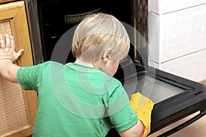 Cleaning dirty oven from grease,food leftovers deposits.Boy child in protective glove,sponge rag washing kitchen stove,helping