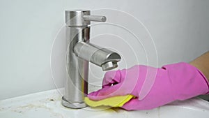 Cleaning the dirty sink and faucet in the bathroom. A woman\'s hand washes the faucet on the sink with a sponge.