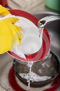 Cleaning dishware kitchen sink sponge washing dish. Close up of female hands in yellow protective rubber gloves washing