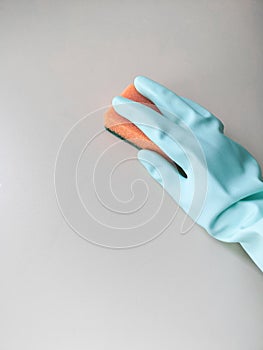 Cleaning and disinfection. A woman in a blue glove holds an orange sponge and washes a light wall