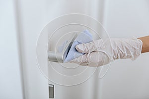 Cleaning door handle with blue wipe in white gloves. Woman hand using towel for cleaning home room door link. Sanitize