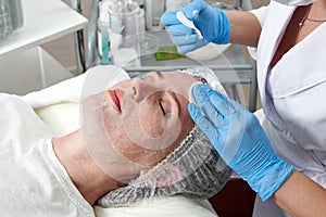 Cleaning face in beauty salon. Cosmetologist removing facial mask from female face