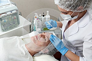 Cleaning face in beauty salon. Cosmetologist removing facial mask from female face