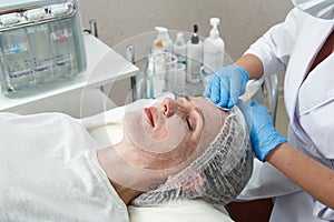 Cleaning face in beauty salon. Cosmetologist removing facial mask from female face