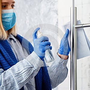 Cleaning front door handle by antibacterial alcohol spray. Woman Houseworker in rubber blue gloves clean Door knob by cloth rag.