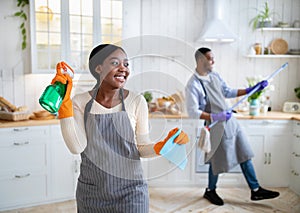 Cleaning is fun. Happy black woman posing with detergent, her husband playing mop like guitar at home, copy space