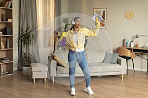 Cleaning is fun. Joyful black maid singing and dancing to music during spring cleanup in modern apartment