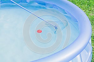 Cleaning of garden swimming pool . Boy tries to cach red ball with Skimmer net