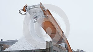 Cleaning of heavy snow on the streets of the city. Municipal urban road maintenance. Close-up of falling snowballs in a truck from