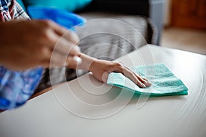 Cleaning home surface with sponge and spray cleaner. Female hands using spray cleaner on white table. Maid wiping dust while